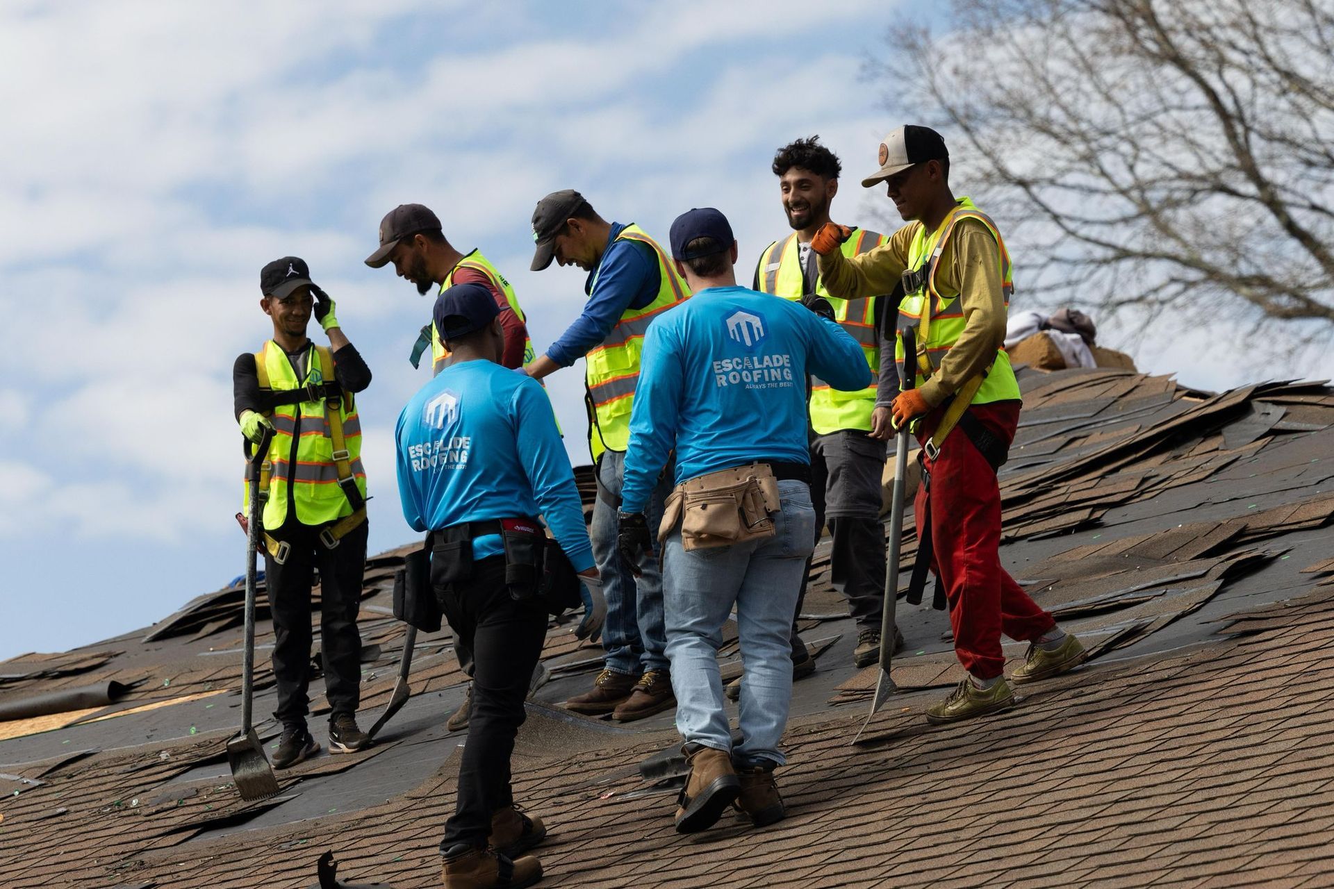 Roofing crew of seven workers wearing safety vests, on a damaged roof.