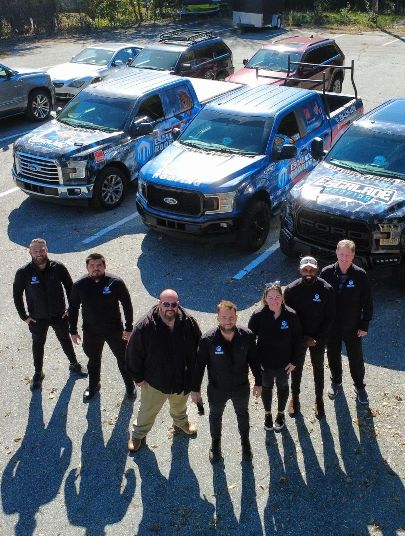 A group of people in black outfits pose with blue trucks in a parking lot.