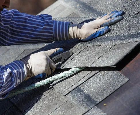Person with gloved hands installing asphalt roof shingles.