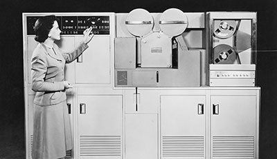 a black and white photo of a woman pointing at a machine