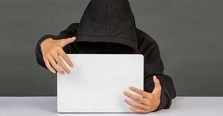 a person in a hoodie is holding a laptop computer .