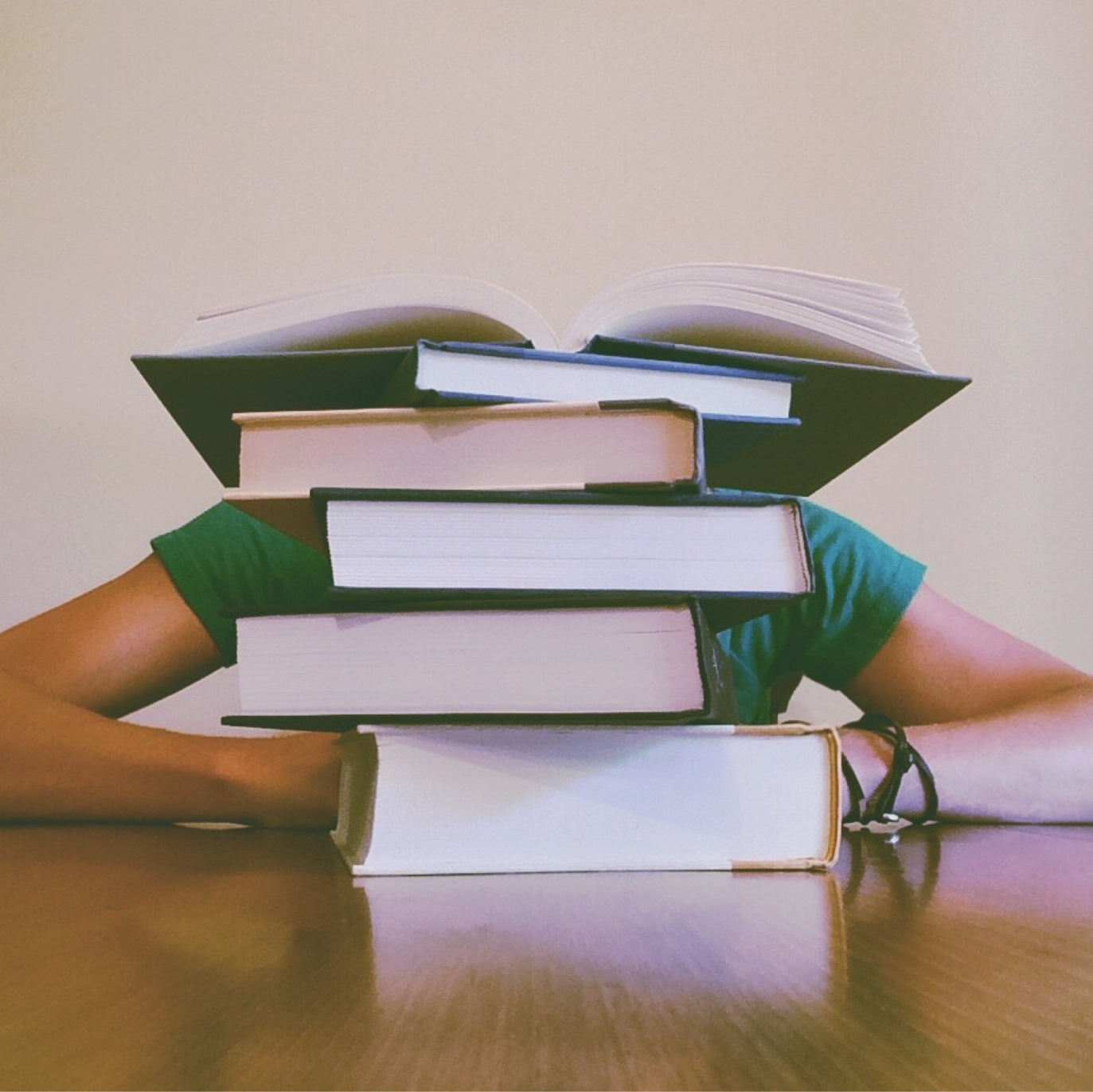 a person sitting at a table with a stack of books covering their face