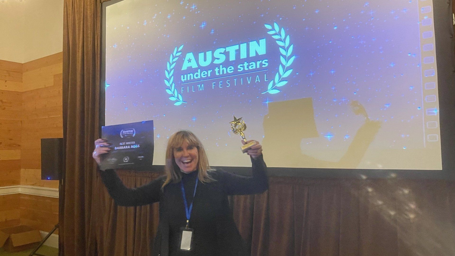 Barbara Ross is holding a trophy in front of a screen that says Austin Film Festival Under the Stars