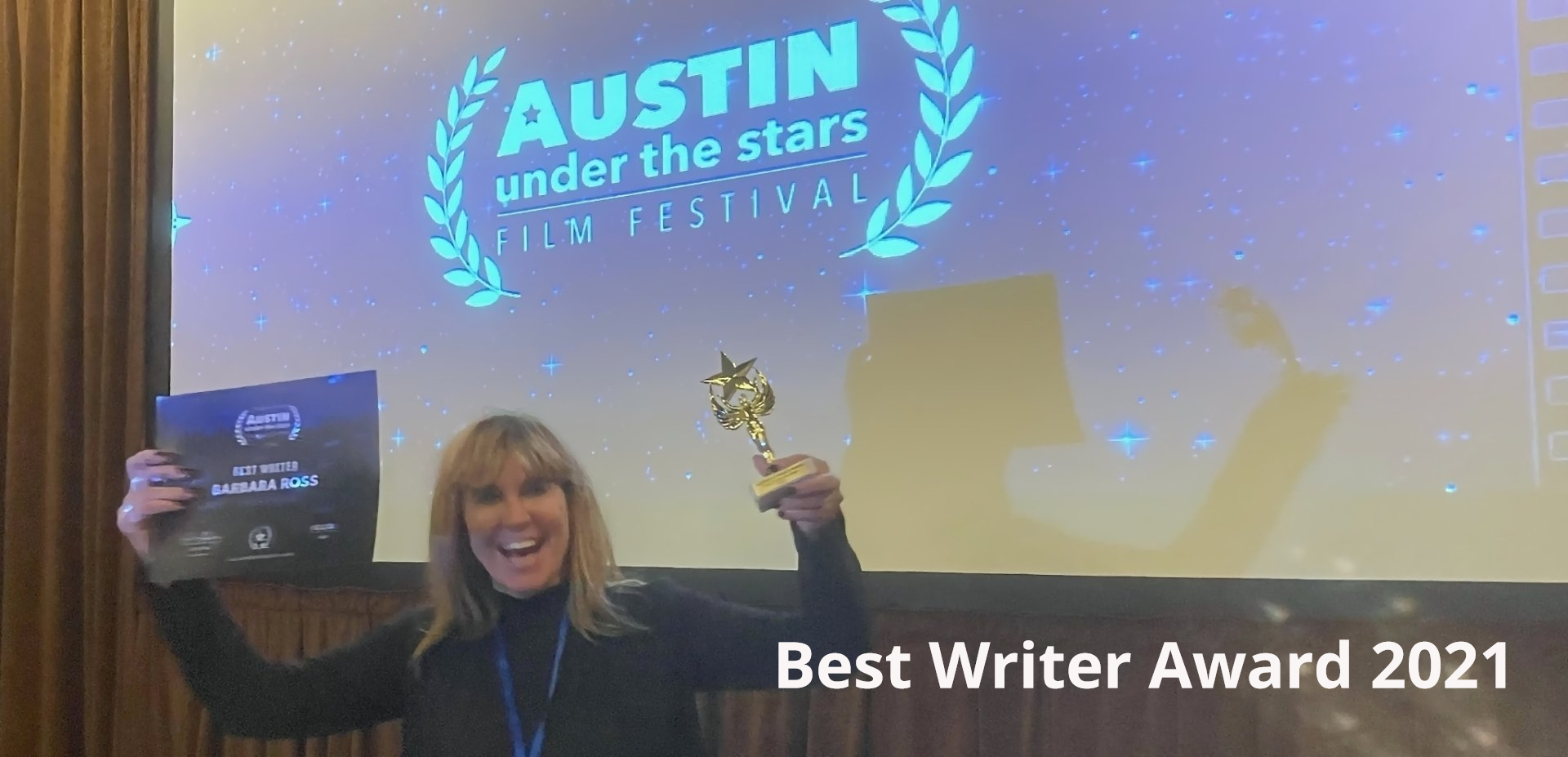 Barbara Ross holds a trophy for best writer in front of a screen that says Austin under the Stars film festival.