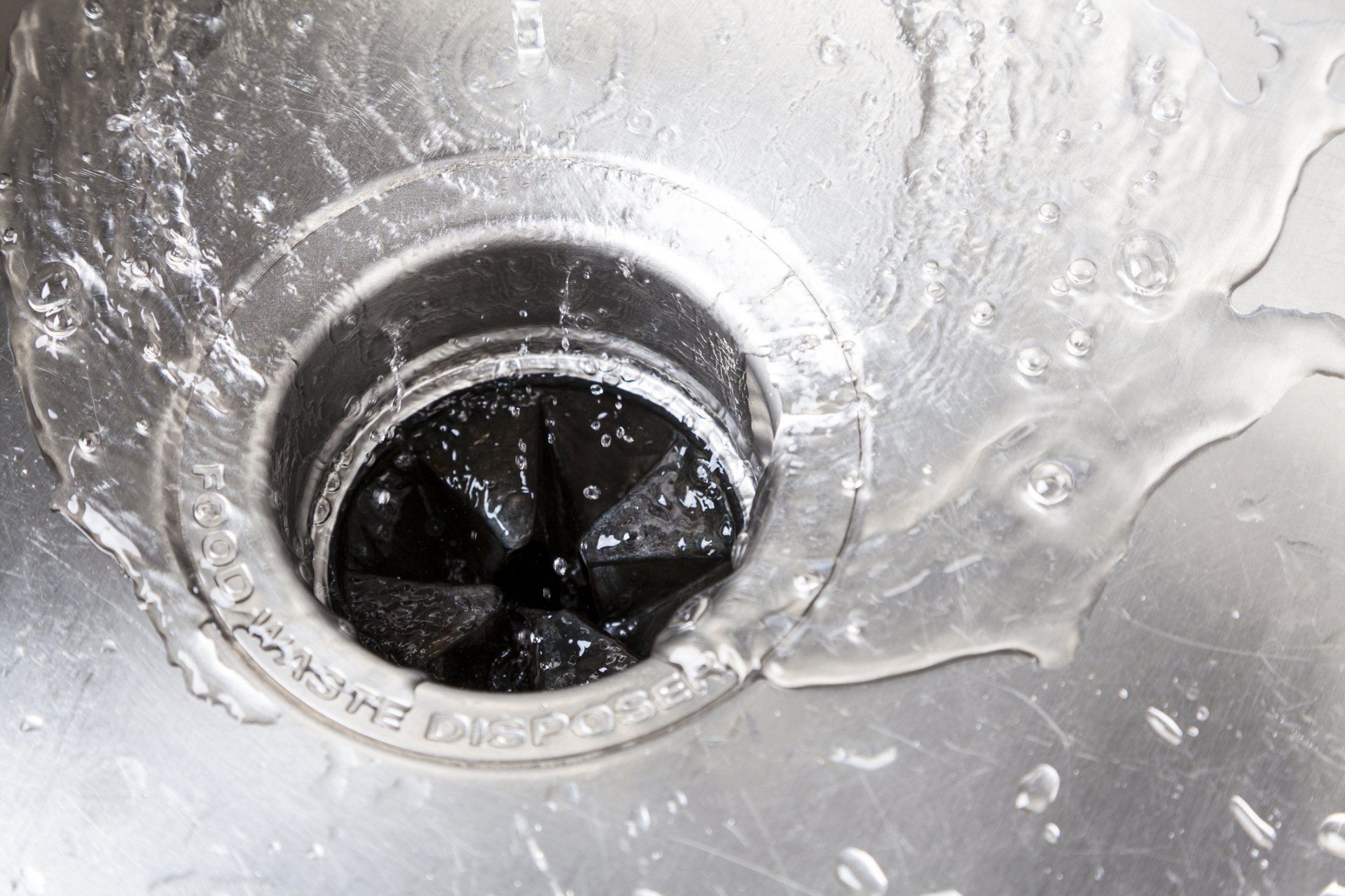 A stainless steel sink with water flowing into the garbage disposal.