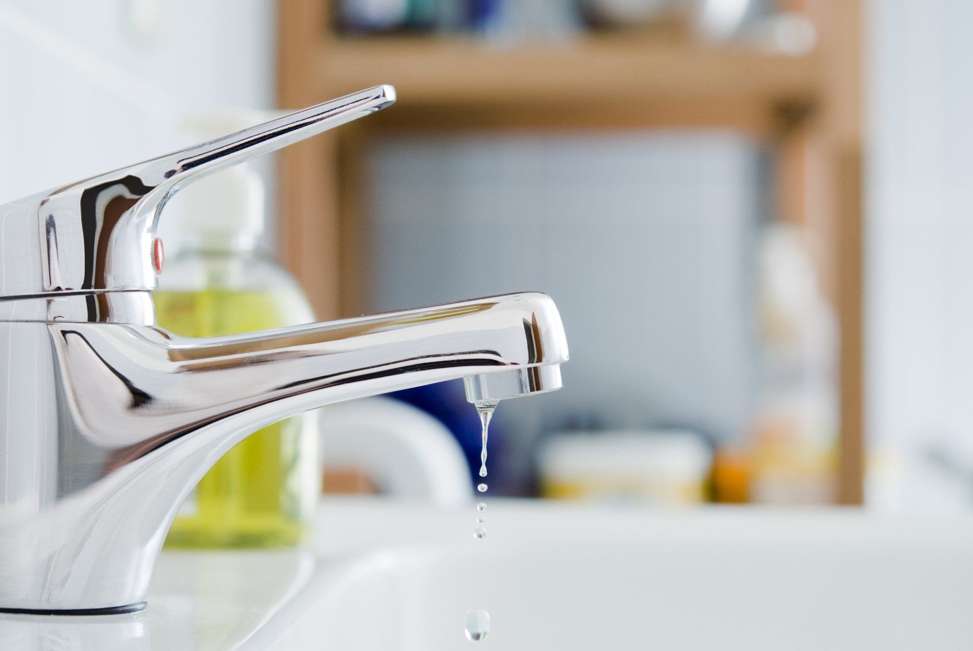 Chrome faucet dripping water into a white sink in a bathroom.