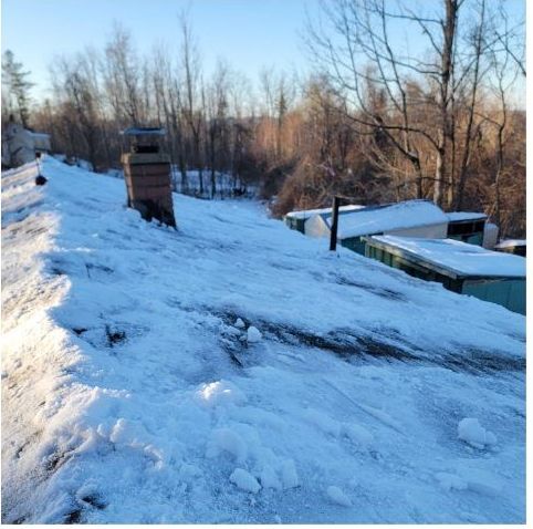 A snowy roof with a chimney and trees in the background