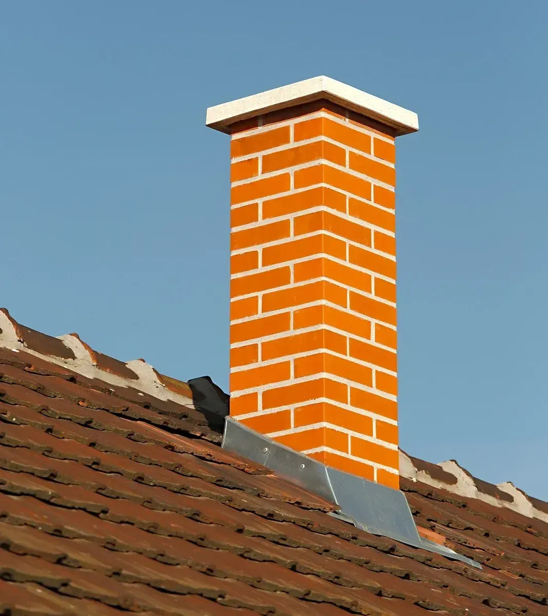 A brick chimney is sitting on top of a tiled roof