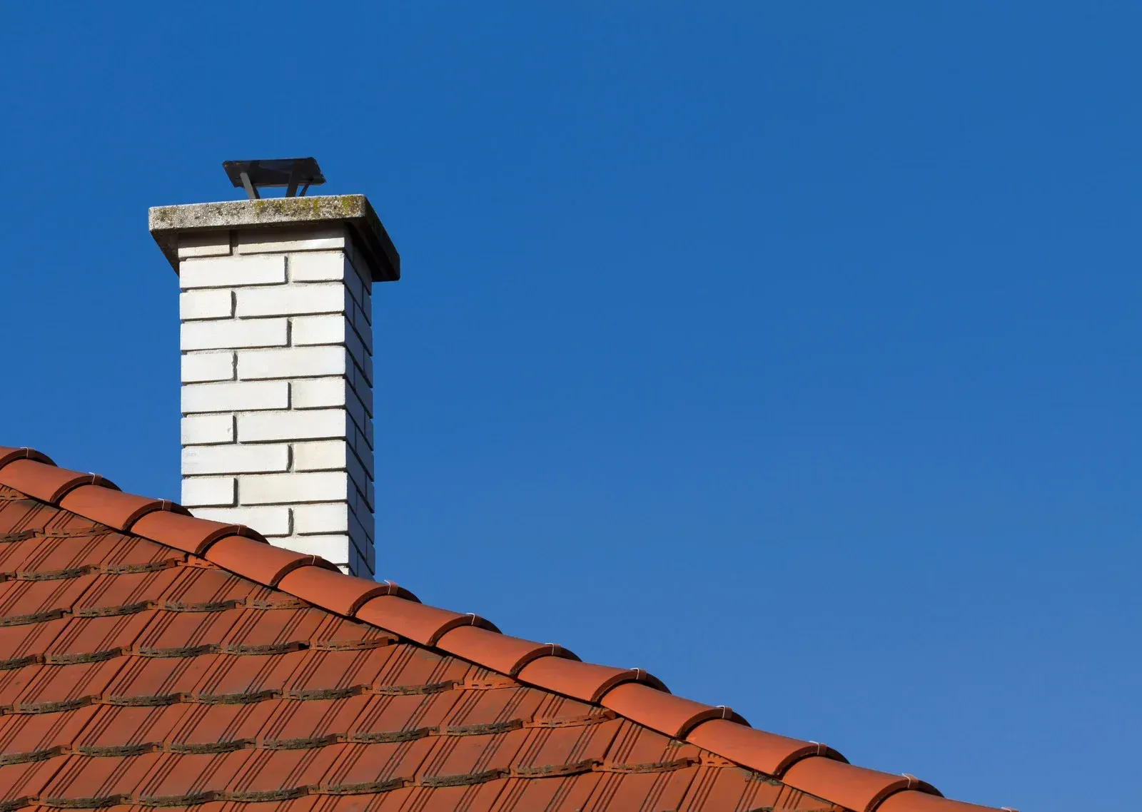 A chimney on top of a tiled roof with a blue sky in the background