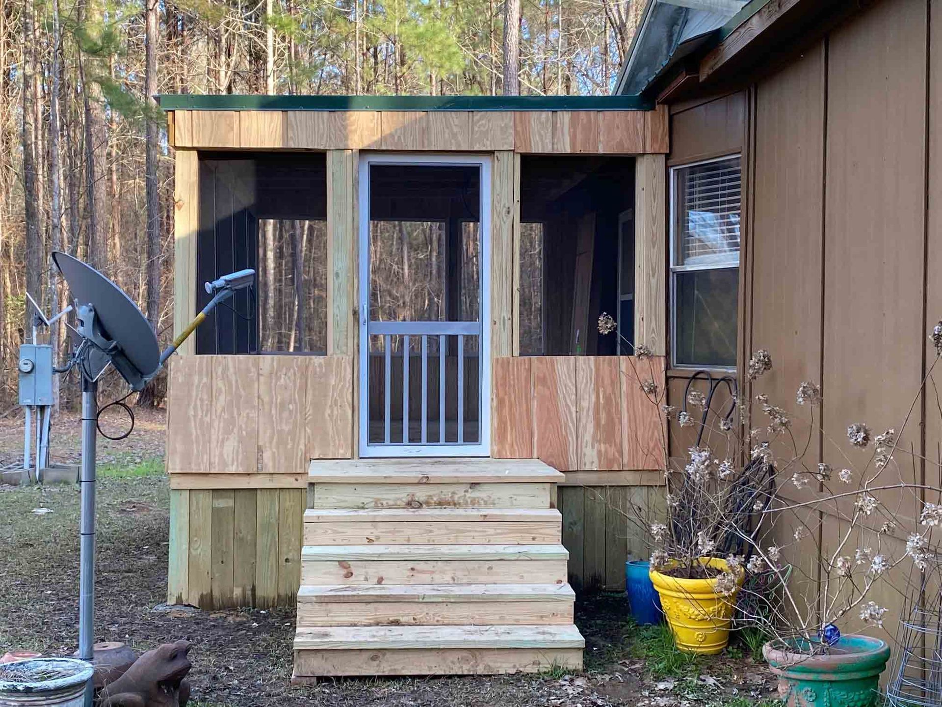 A brown home addition with a screen door and wooden stairs leading up to it, positioned next to a brown exterior wall.