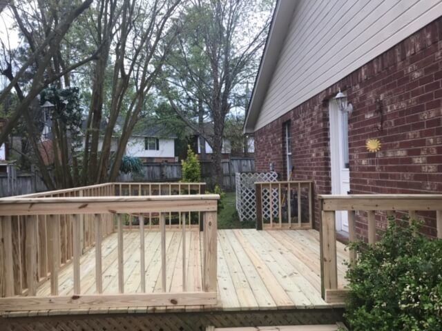 A newly built light wood deck with railings attached to the brick exterior of a house, overlooking a grassy backyard.