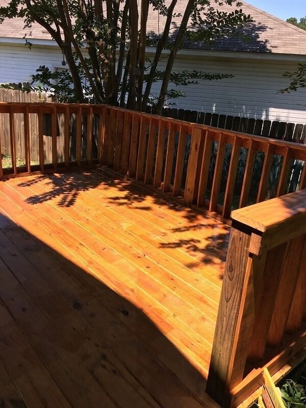 A freshly stained, light-brown wooden deck with railing, seen from an elevated angle on a sunny day.