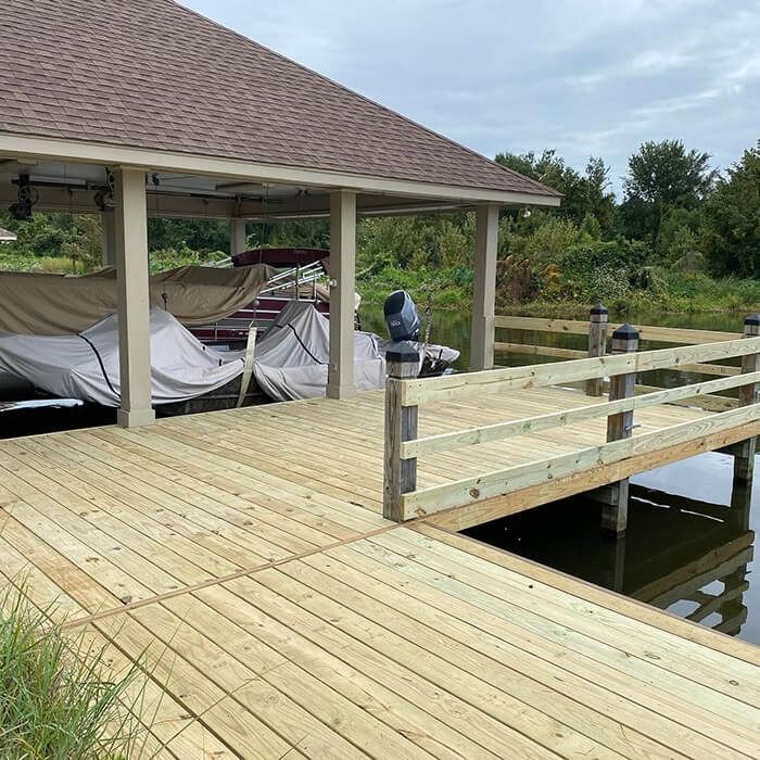 A newly built wooden boat dock with a covered slip and railings extending over calm water near a treeline.