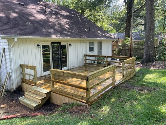 A newly built wooden deck with railings and stairs attached to the back of a light-colored house in a grassy yard.