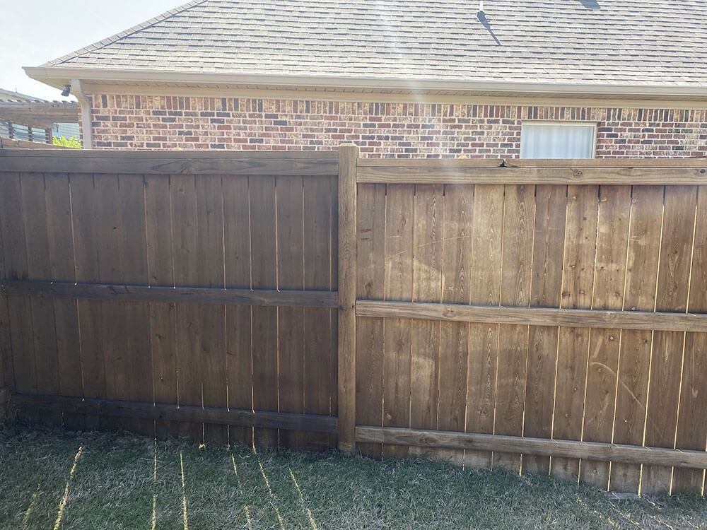 A split-view image showing a section of a wooden fence being power washed, with the left side clean and the right side dirty.