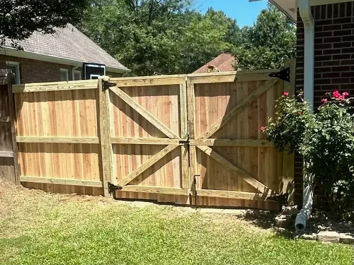 A wooden double gate for a backyard fence, featuring diagonal cross-bracing, next to a brick house wall.