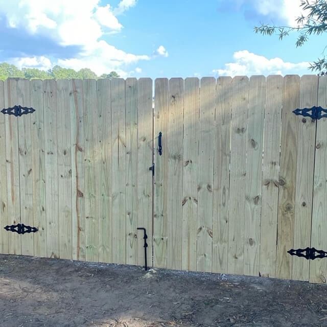 A wooden double gate with black hinges and a central latch, set against a blue sky.