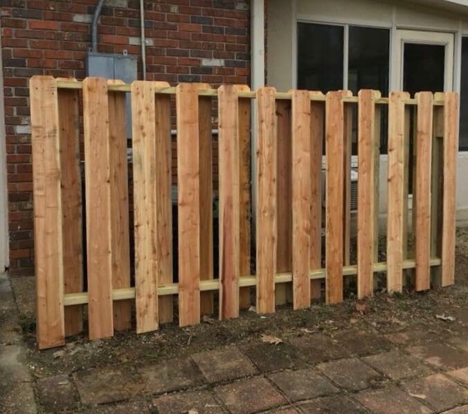 A cedar privacy fence standing on a paved patio against a brick house wall.