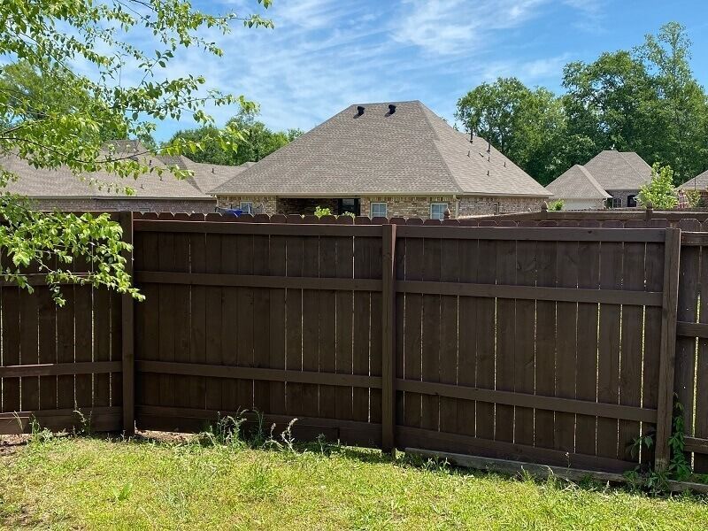 A wooden fence spans the foreground with a residential backyard, neighboring homes, and trees visible in the background.