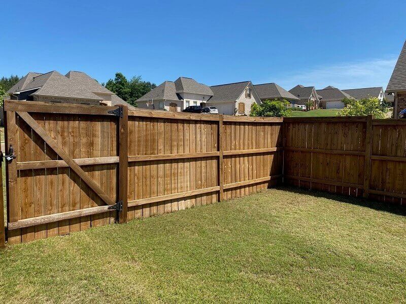 A sturdy wooden privacy fence with a gated section encloses a green lawn under a clear blue sky.