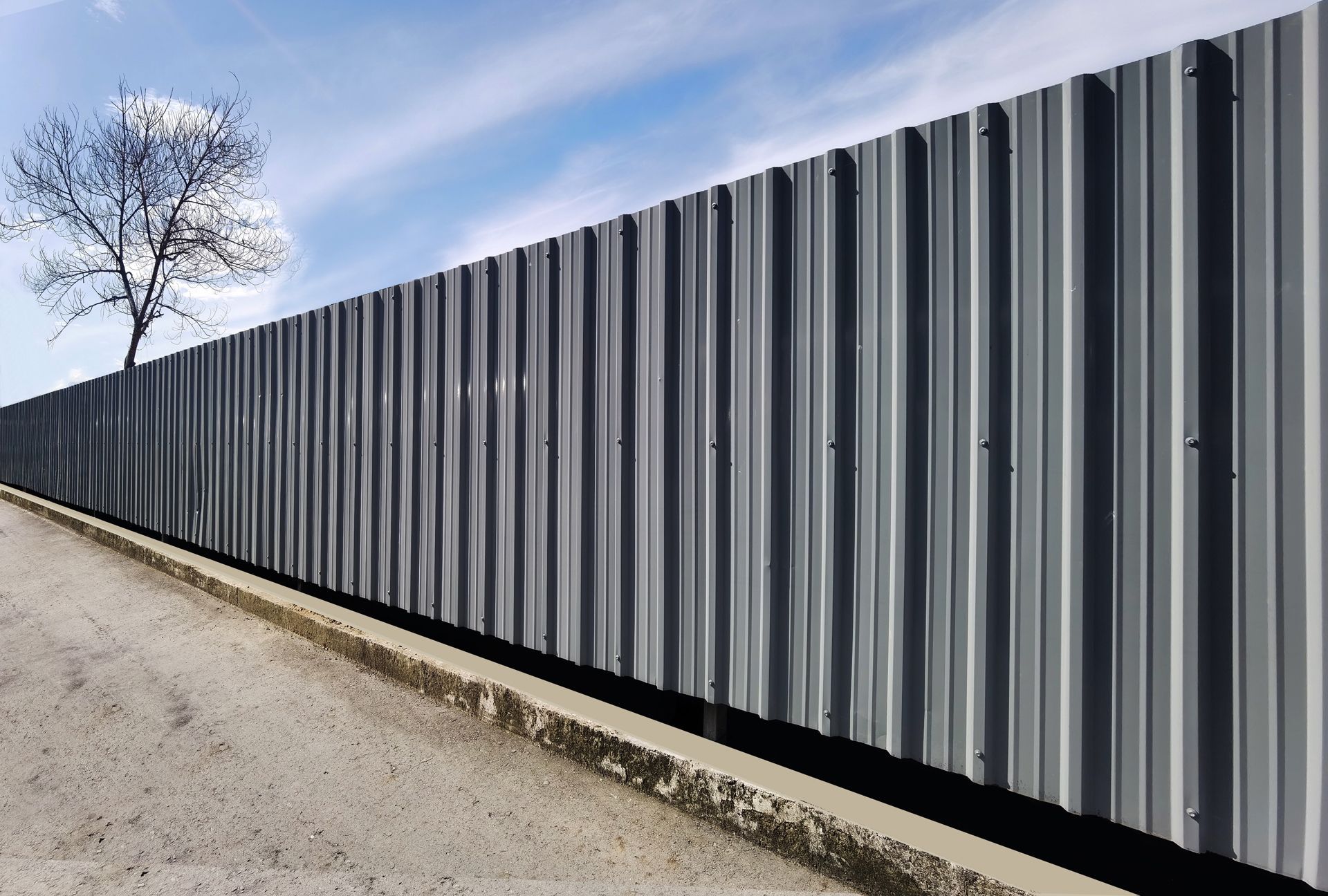 A tall, corrugated grey metal fence stands along a concrete curb.