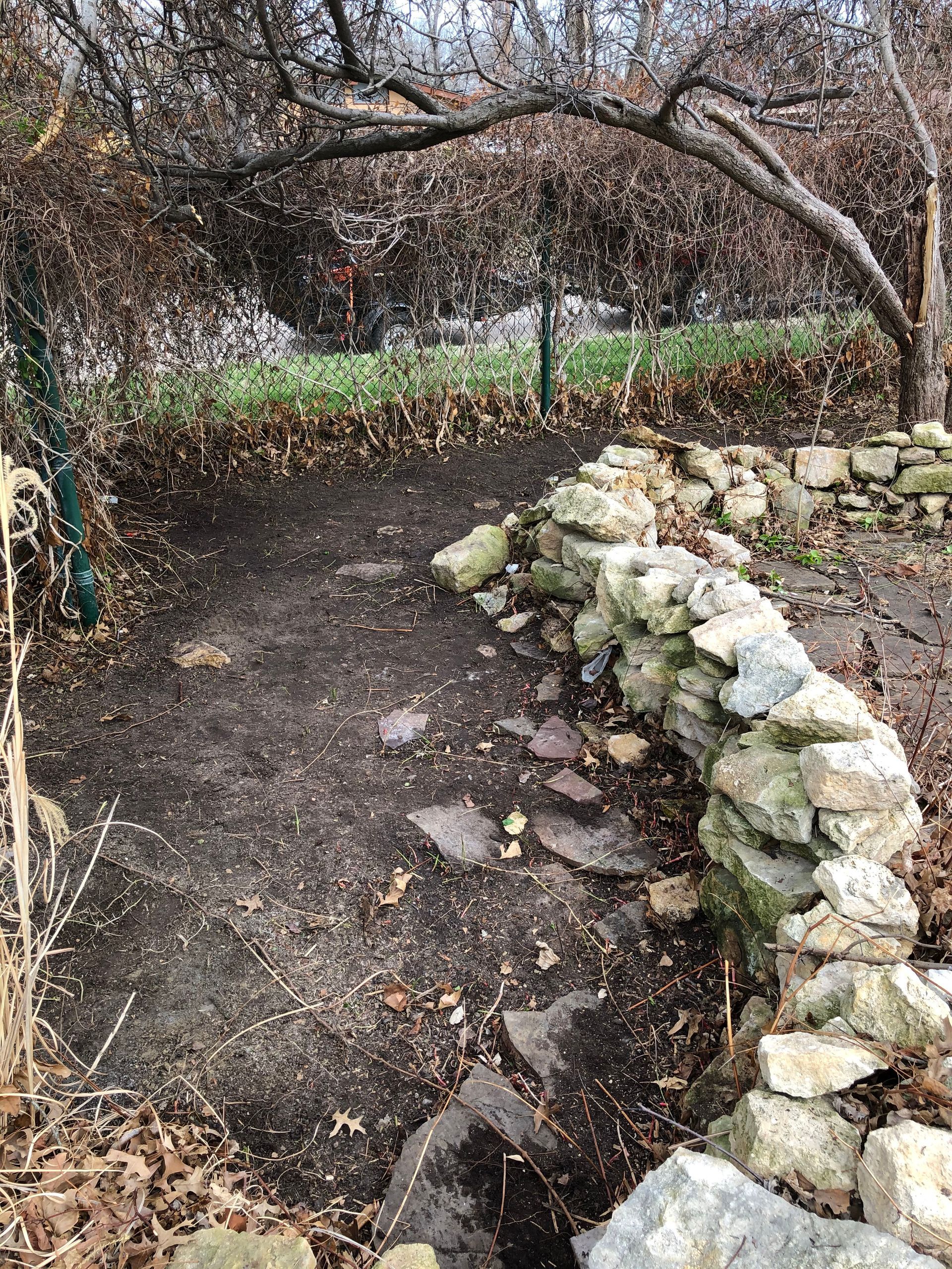 a stone wall surrounds a dirt path in a garden .