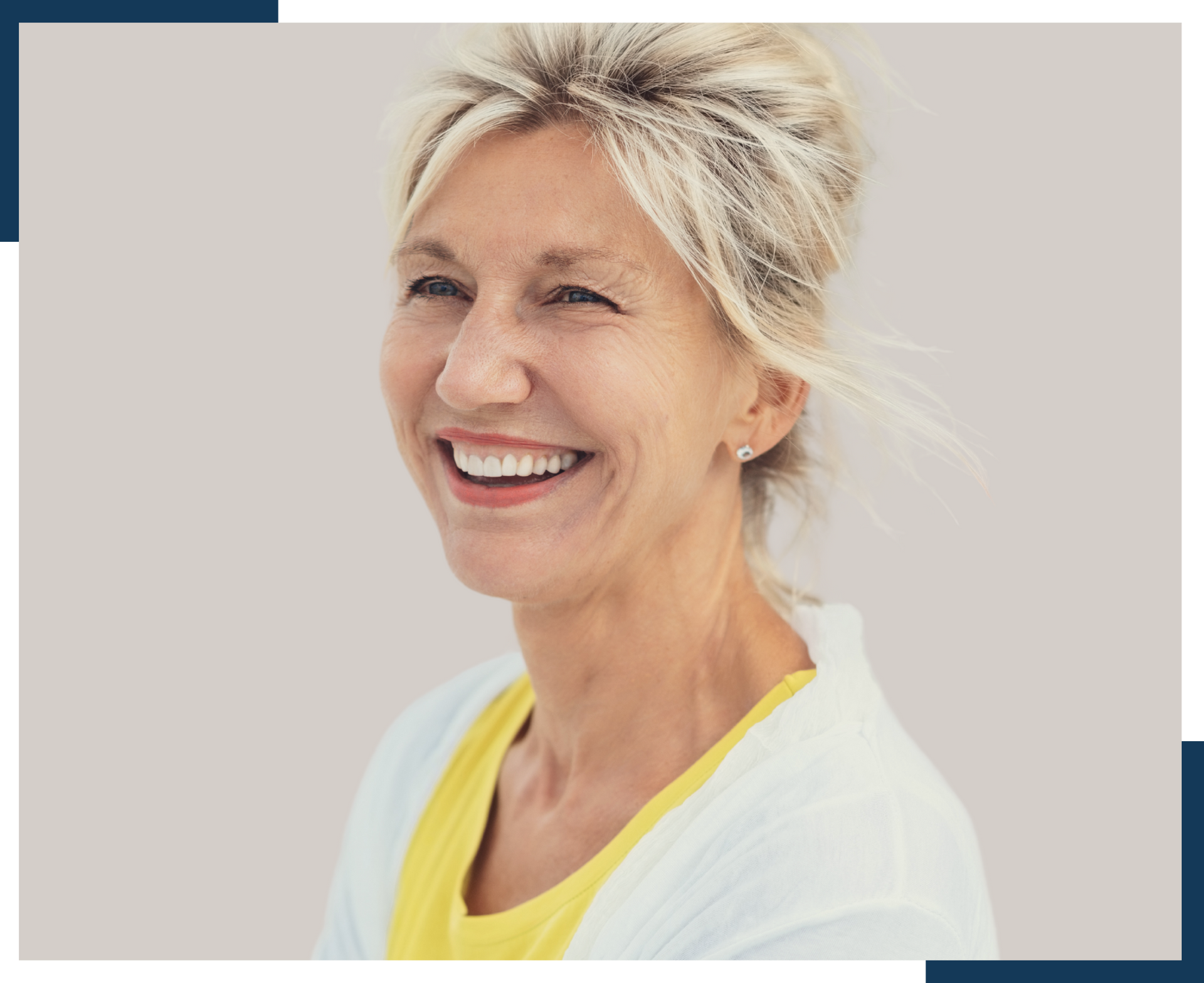 An older woman is smiling and wearing a yellow shirt and a white sweater.