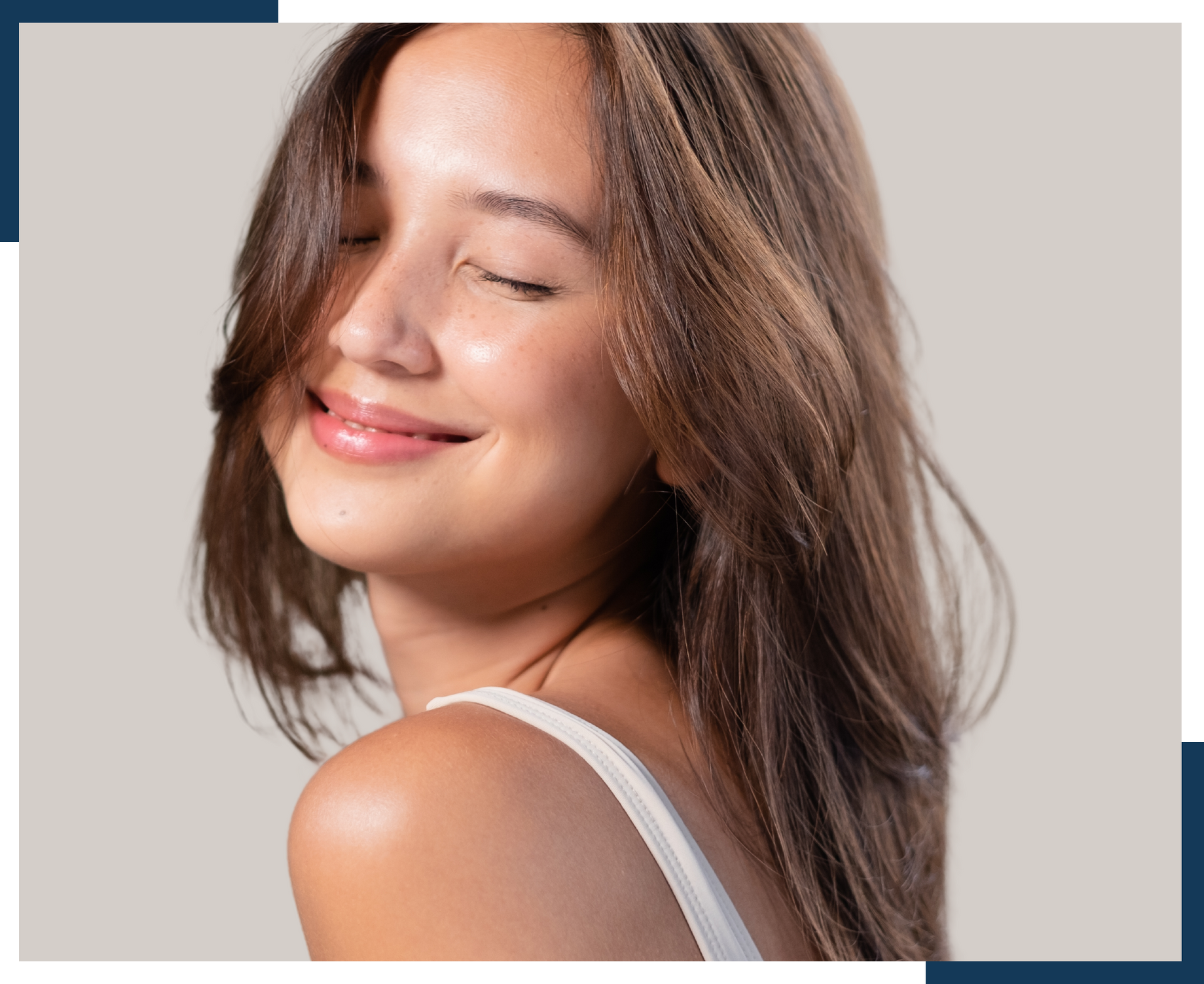 A woman with long brown hair is smiling with her eyes closed.