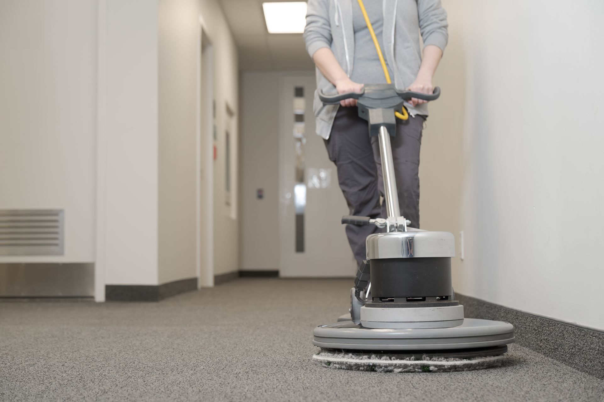 Person using a floor buffer to clean a carpeted hallway.