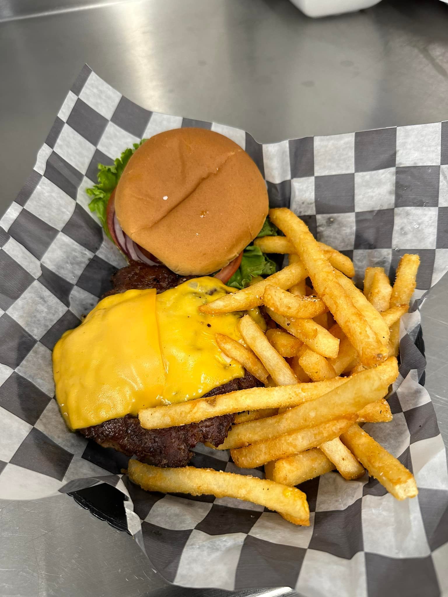 A hamburger and french fries on a checkered paper on a table.