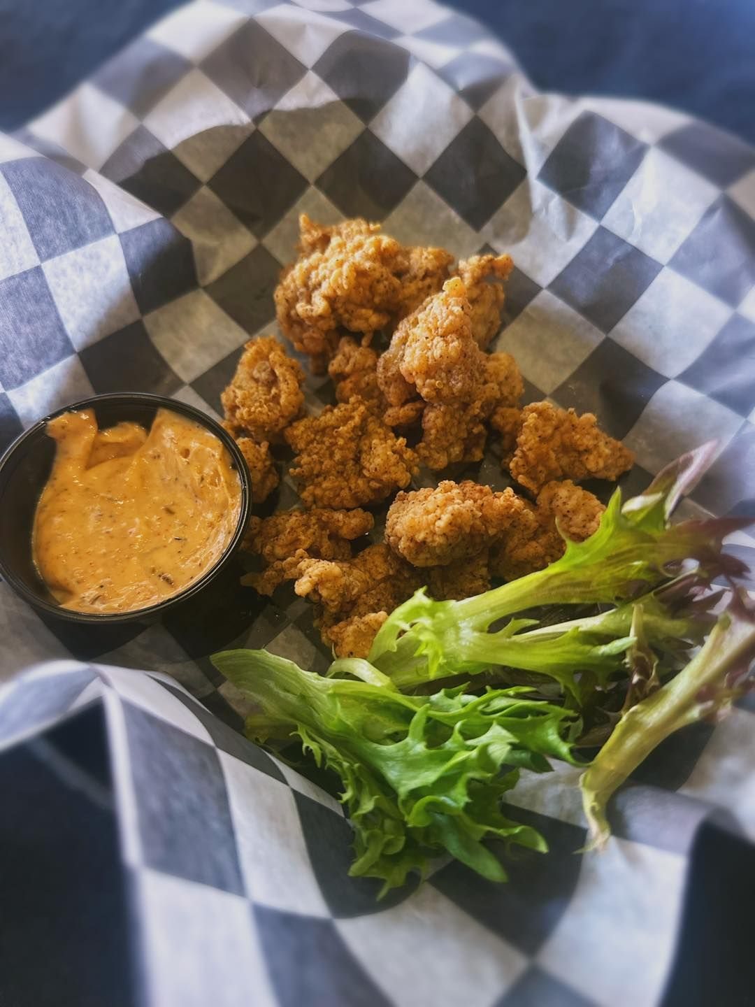 A basket of fried chicken and lettuce on a checkered napkin.