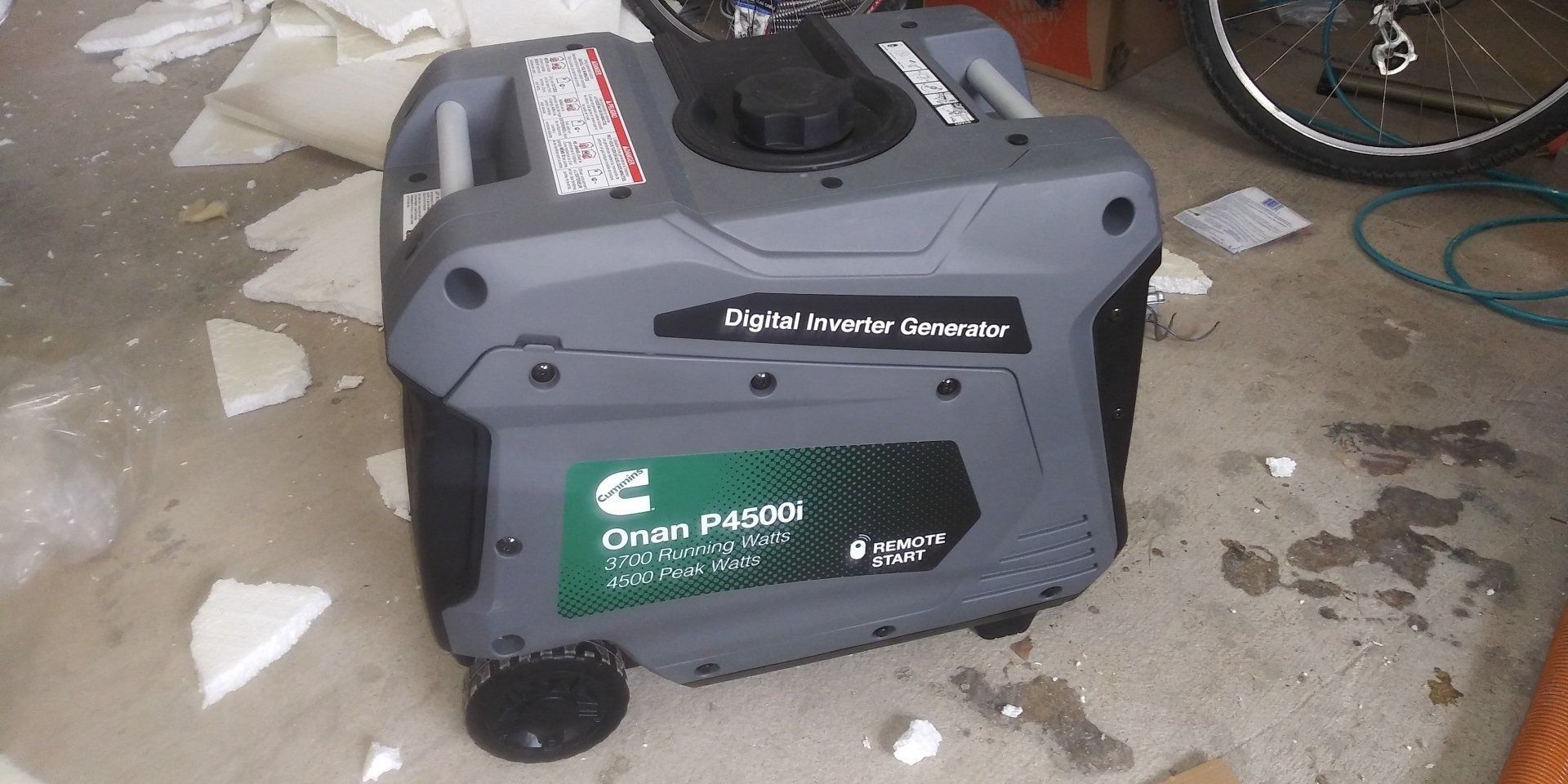A generator is sitting on the ground in a garage next to a bicycle.
