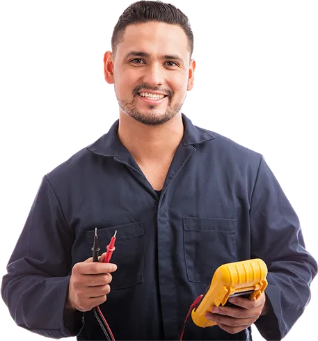 A man in a blue jumpsuit is holding a multimeter and smiling.