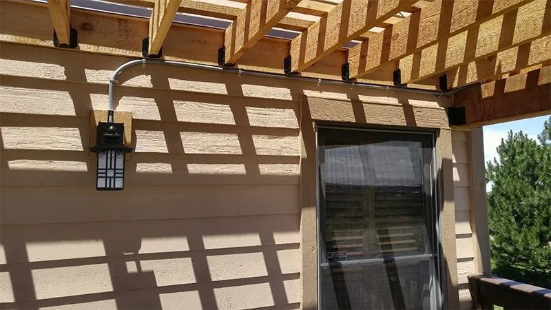 A wooden pergola is covering a patio with a sliding glass door.
