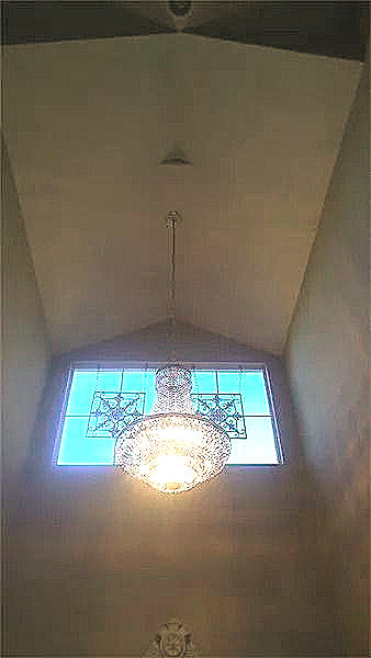 A chandelier is hanging from the ceiling in front of a stained glass window.
