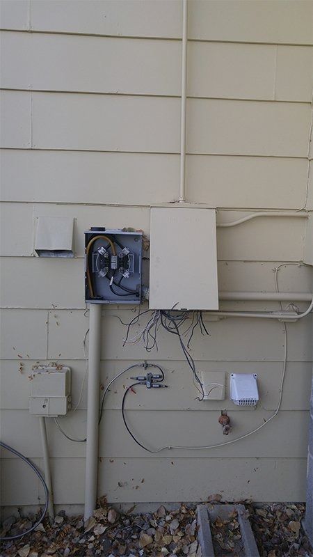 There is a box on the side of a house with wires coming out of it.