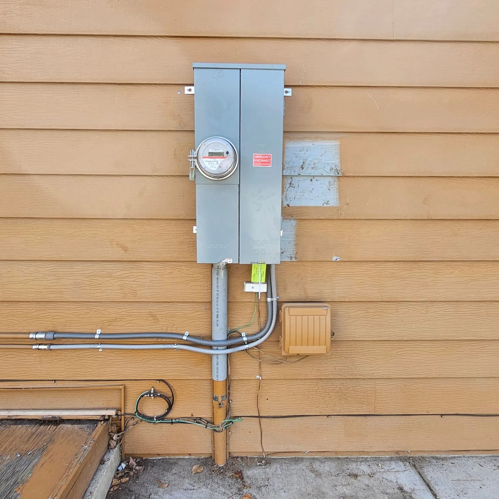 An electrical box is attached to the side of a wooden house.