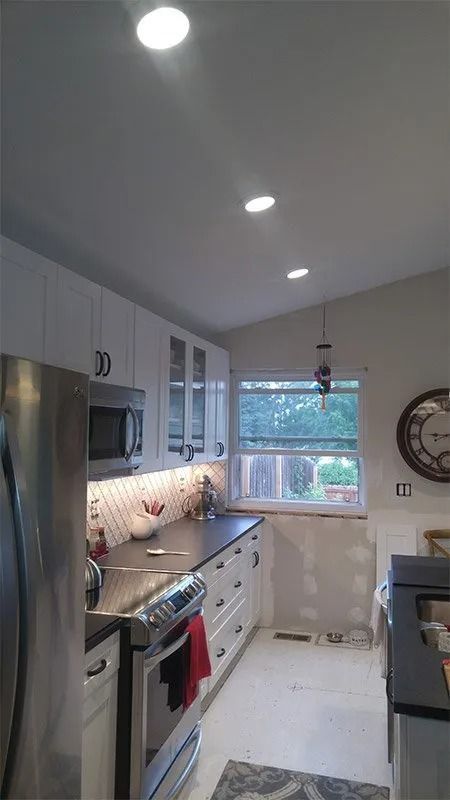 A kitchen with white cabinets , stainless steel appliances , a refrigerator and a window.