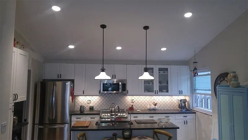 A kitchen with white cabinets and stainless steel appliances and two pendant lights hanging from the ceiling.