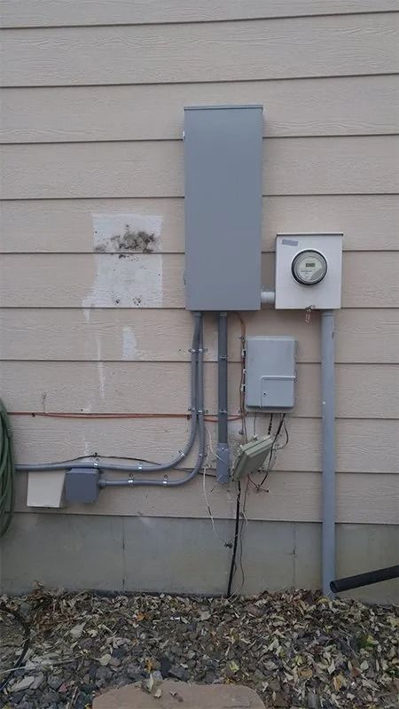 A electrical box is attached to the side of a house.
