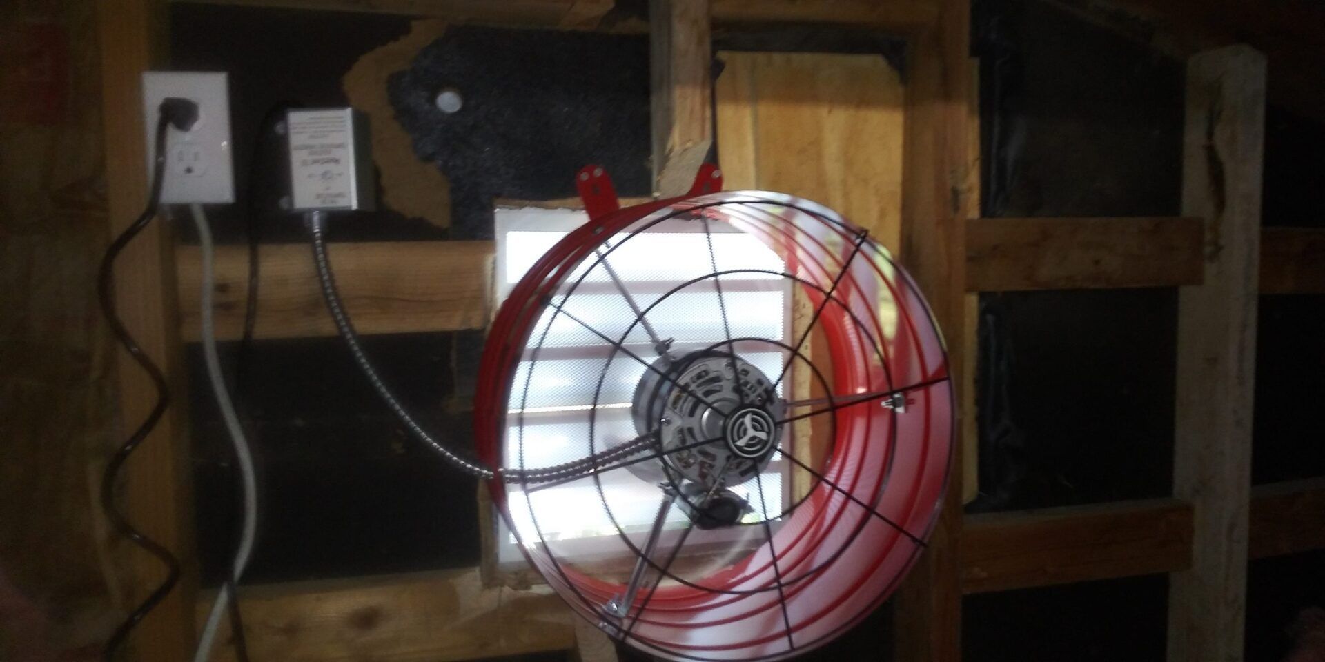 A red fan is hanging from a wooden wall.