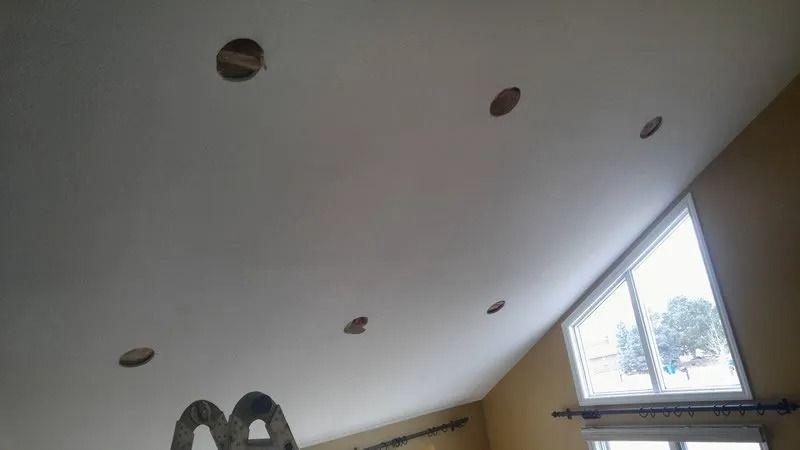 A person is standing on a ladder in a living room looking up at the ceiling.