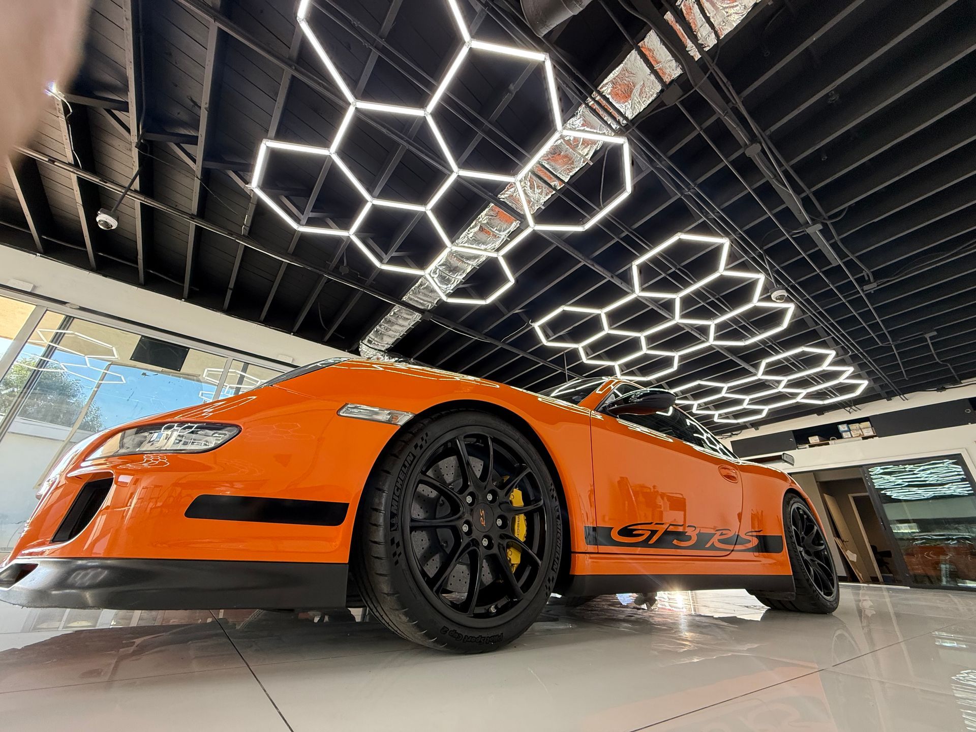 Orange sports car in a showroom under geometric ceiling lights