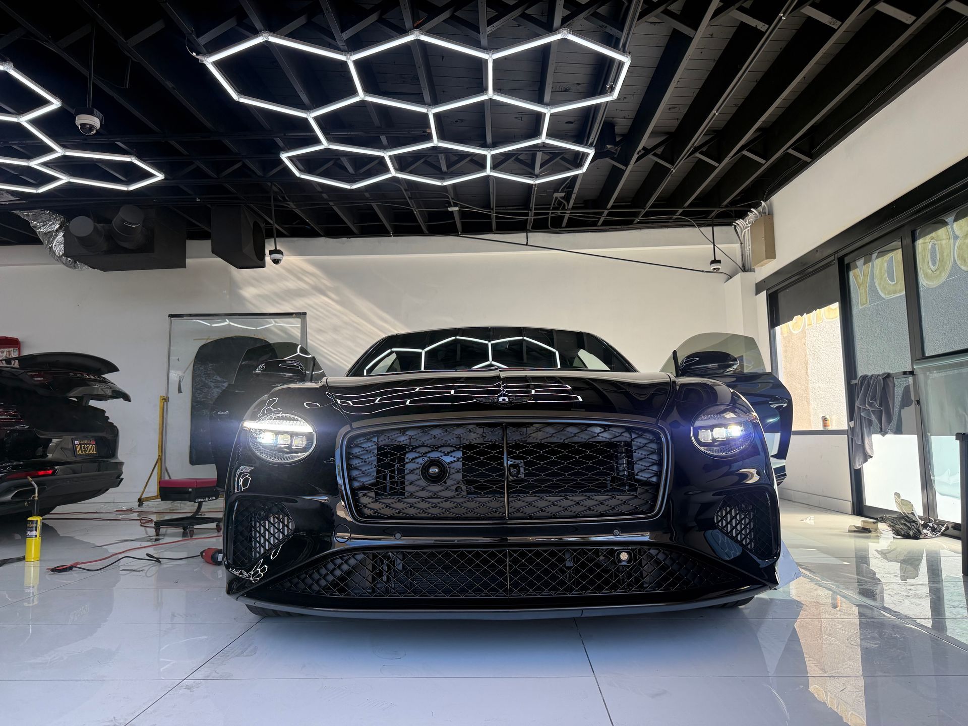 Black sports car in a garage with geometric ceiling lights and a glossy floor
