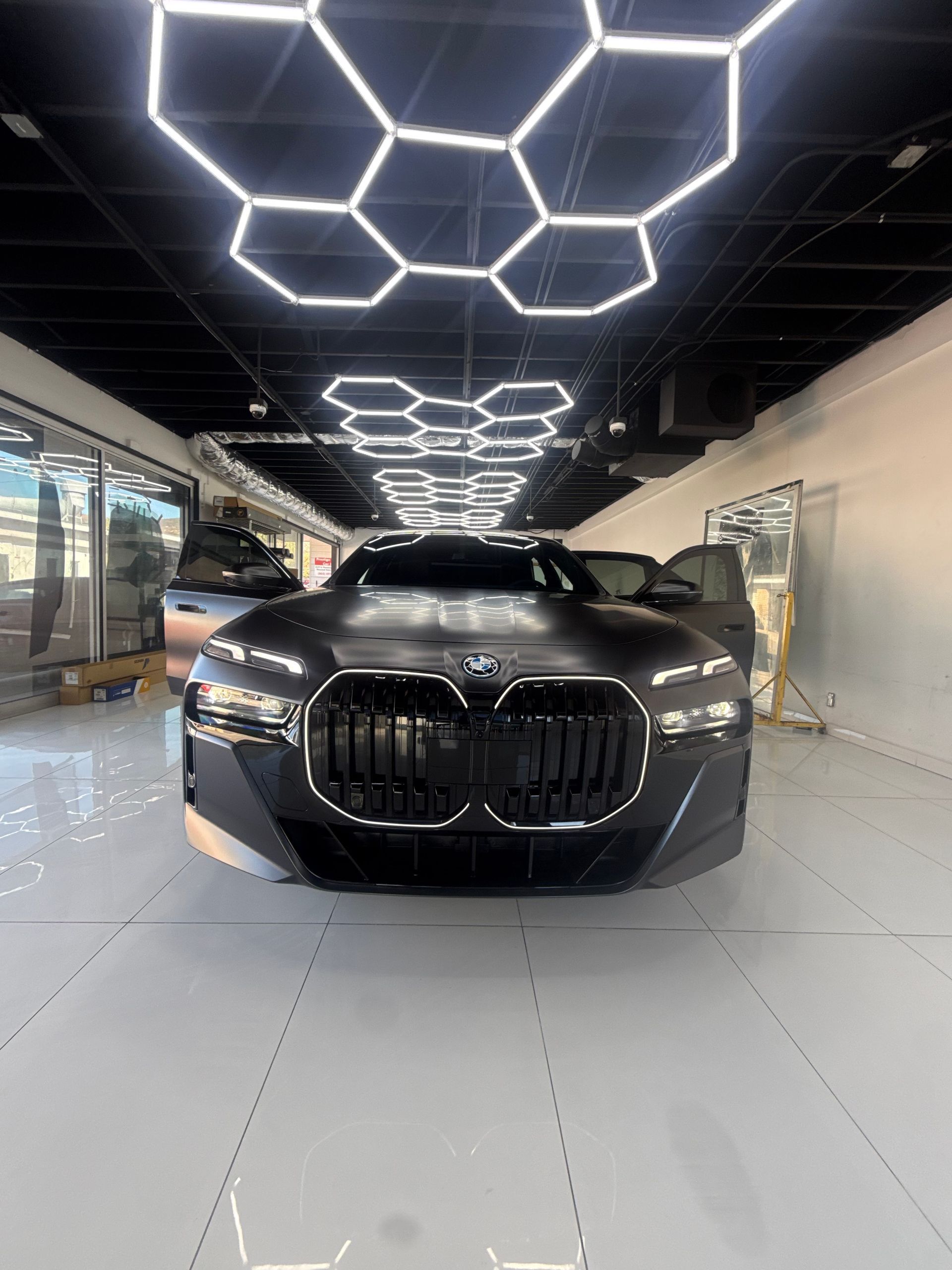 Black luxury sedan in a showroom with geometric ceiling lights.