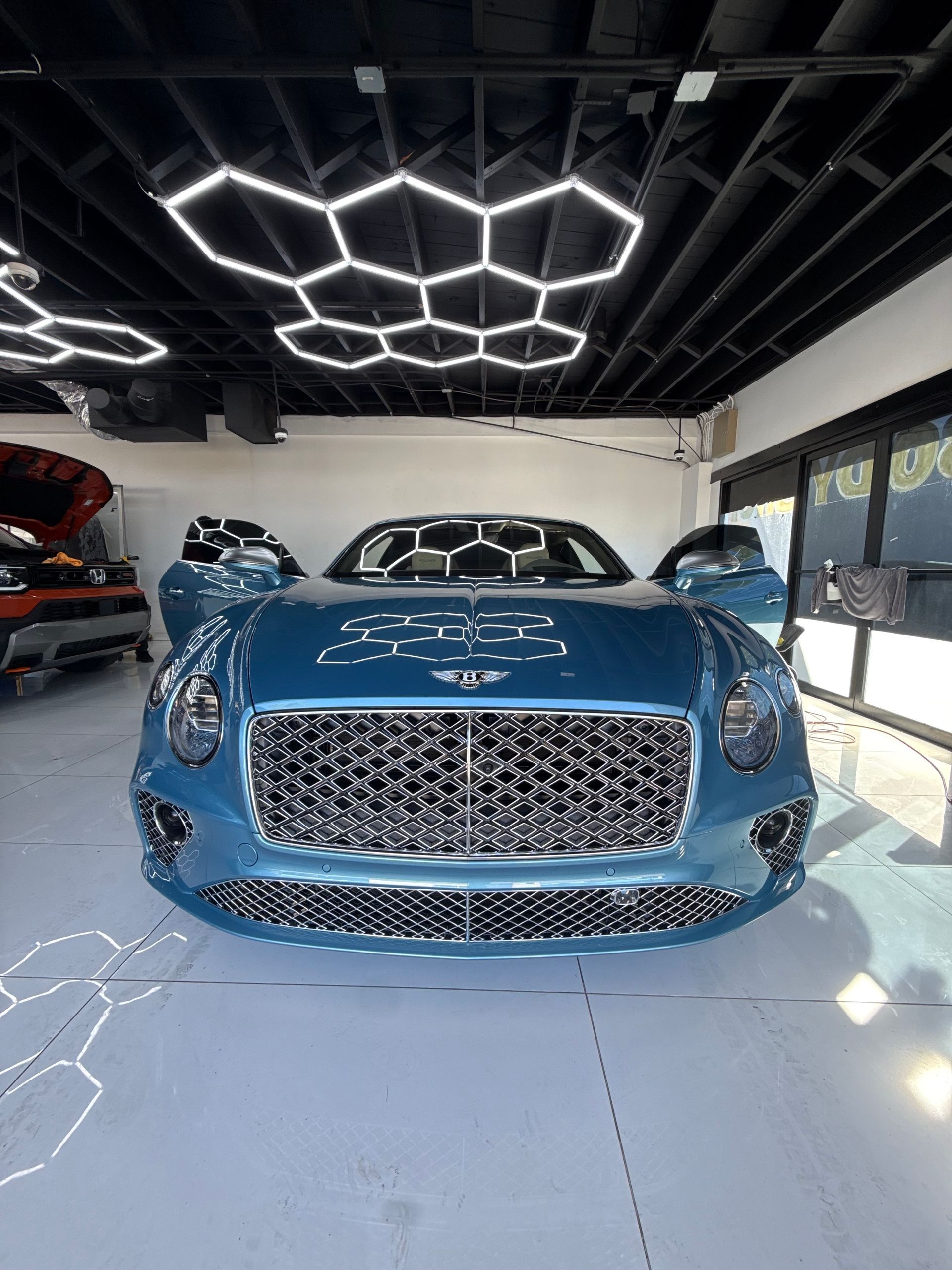 Blue luxury car in a showroom with geometric ceiling lights and glossy floor