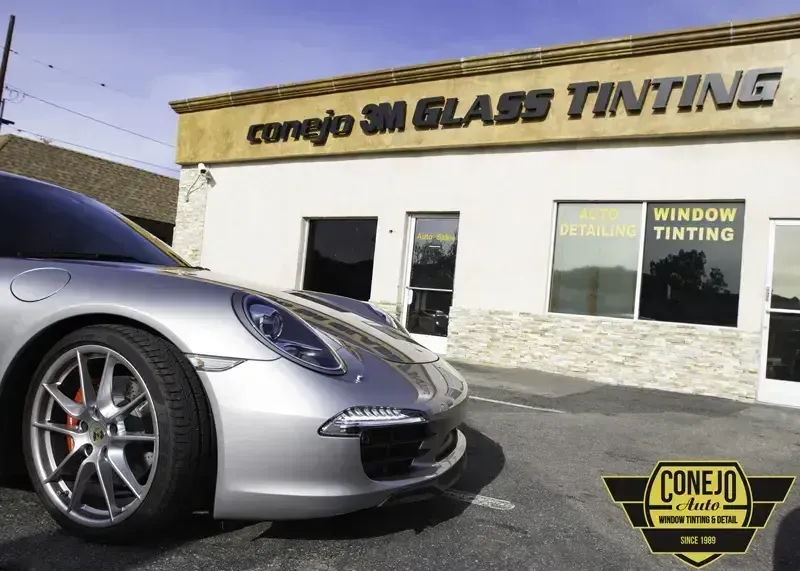 Silver sports car parked outside Conejo Simi Glass Tinting storefront with “Window Tinting” sign