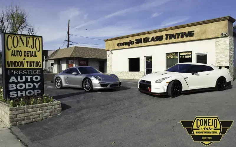 Two sports cars parked outside Conejo Auto Body Shop on a sunny day