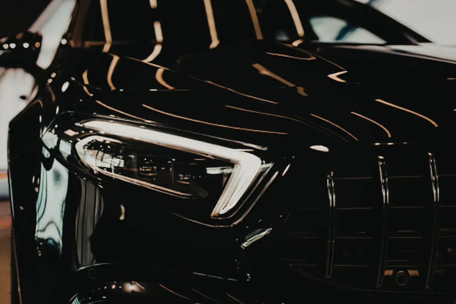 Close-up of a glossy black car front headlight with reflections on the hood