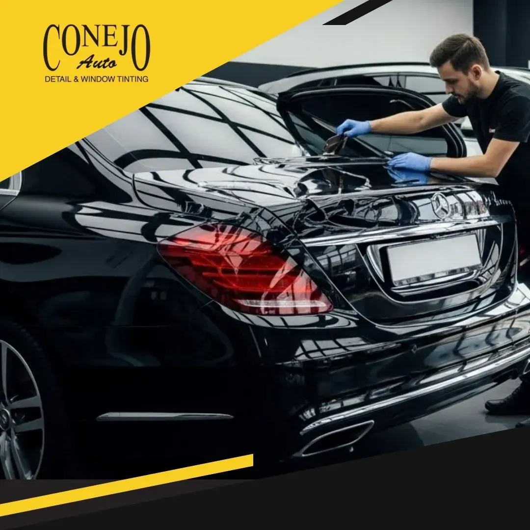 Detailer polishing a black car in a garage, with a yellow Conejo Auto logo in the corner